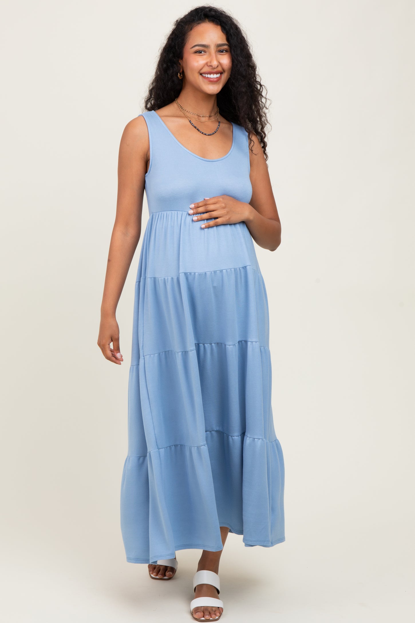 woman wearing a light blue sleeveless maternity maxi dress and holding her baby bump