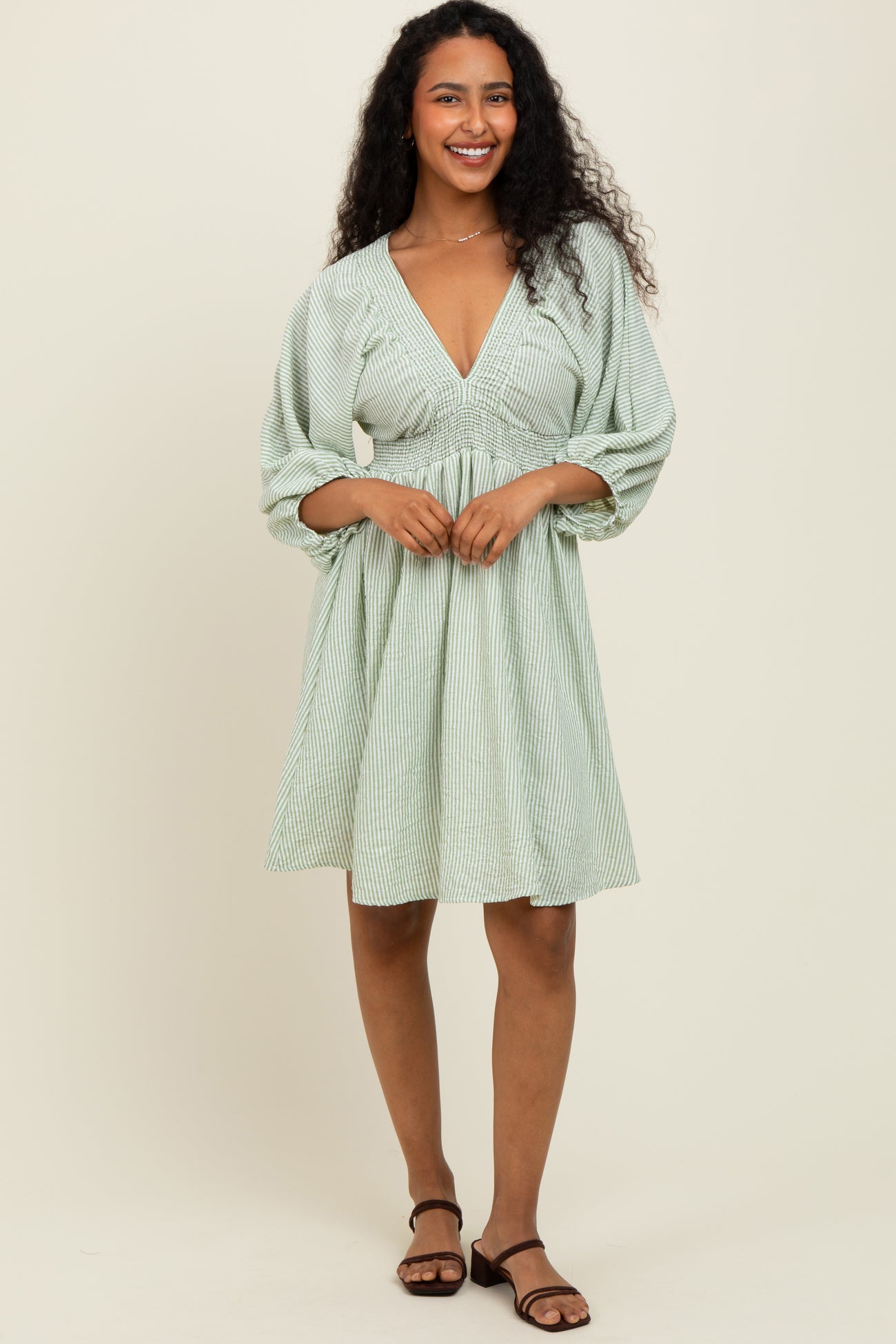 woman wearing a green striped short sleeve dress with a deep v-neck and gathered waist holding the skirt