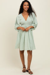woman wearing a green striped short sleeve dress with a deep v-neck and gathered waist holding the skirt