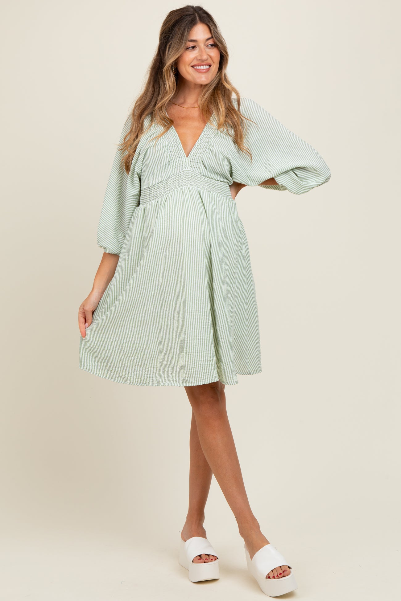 woman wearing a green and white striped maternity dress with a v-neck and balloon sleeves, showing her baby bump
