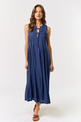 woman wearing a sleeveless navy blue maxi dress with pleated detailing and a tie neckline