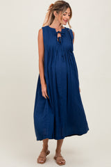 woman wearing a navy blue sleeveless maternity dress with pleats and a tie detail, showing her baby bump