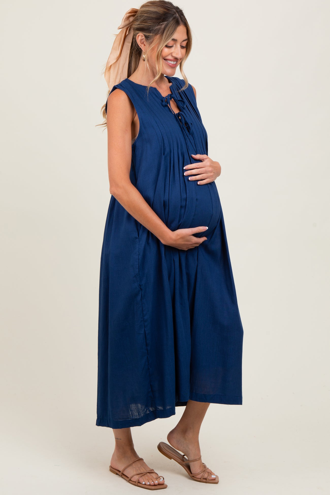 woman wearing a navy blue sleeveless maternity dress with a tie detail, showcasing her baby bump