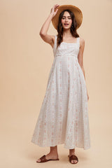 woman wearing a flowy white maxi dress with floral stripes and a wide-brimmed straw hat