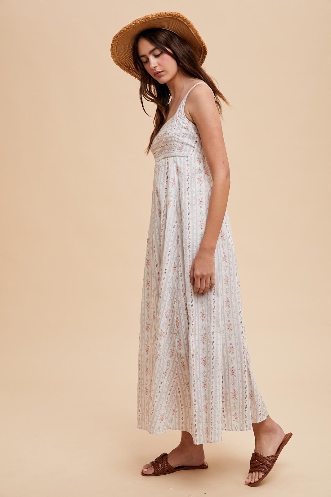 woman wearing a light beige floral maxi dress and a wide-brimmed straw hat, standing in profile
