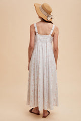 woman wearing a long white floral maxi dress with adjustable straps and a straw hat, seen from the back