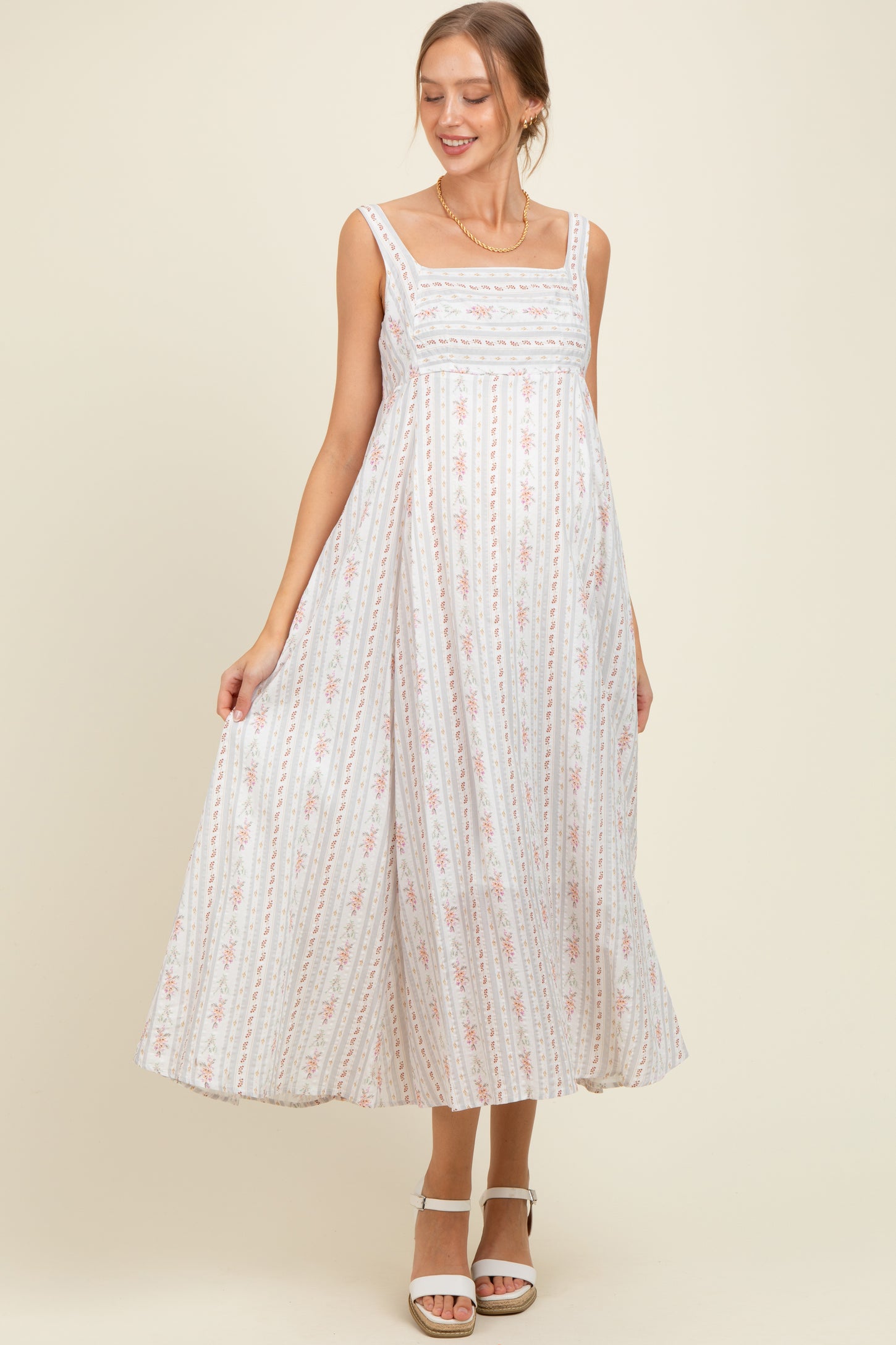 woman wearing a white floral print maternity maxi dress with a square neckline and a visible baby bump