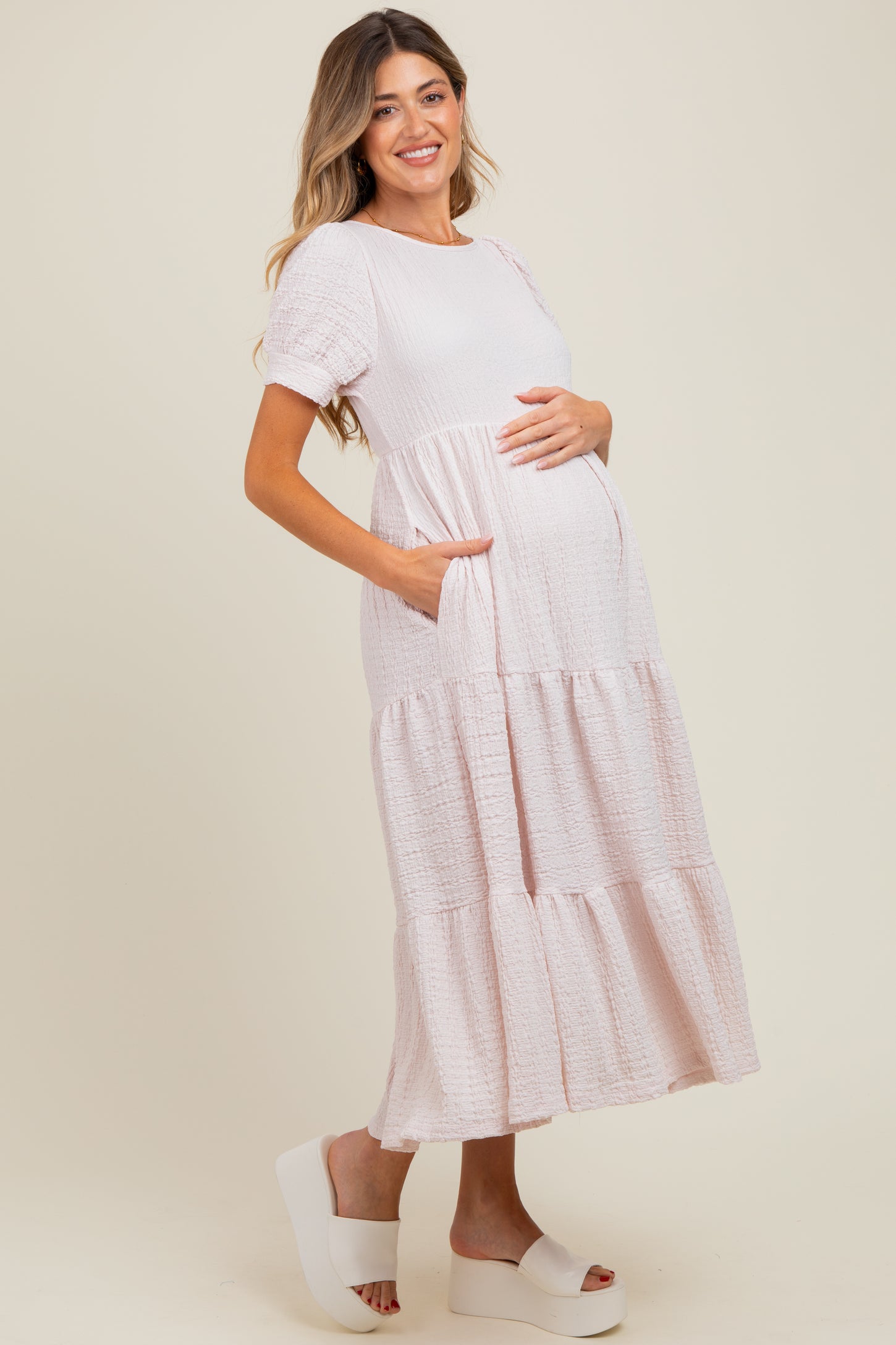 woman wearing a light pink tiered maternity dress with pockets and holding her baby bump