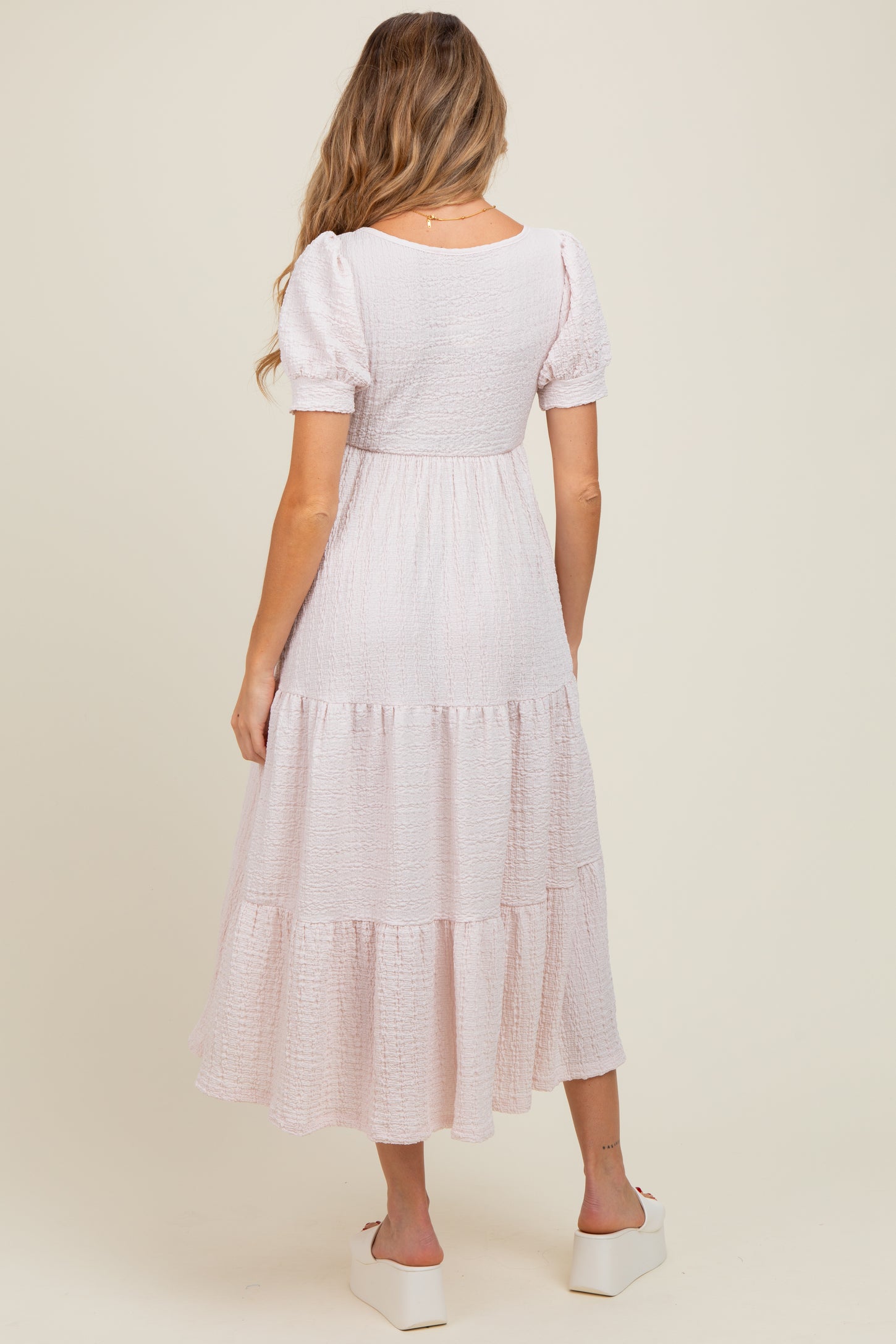 woman wearing a light pink maternity tiered maxi dress with puff sleeves and a scoop back, showing a baby bump