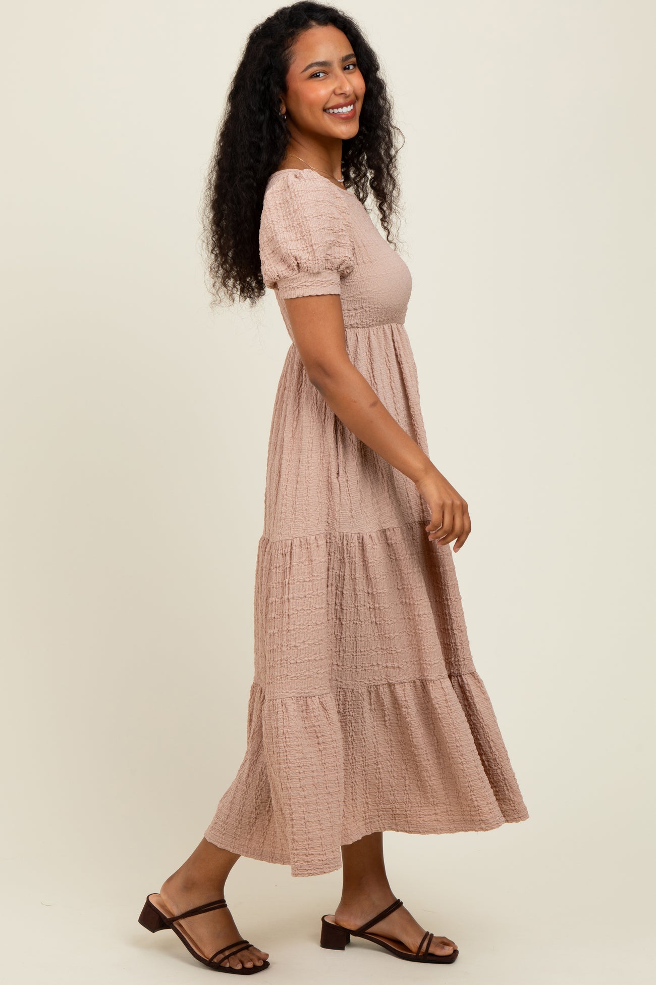 woman wearing a blush pink tiered maxi dress with short puff sleeves and a relaxed fit, standing sideways and smiling