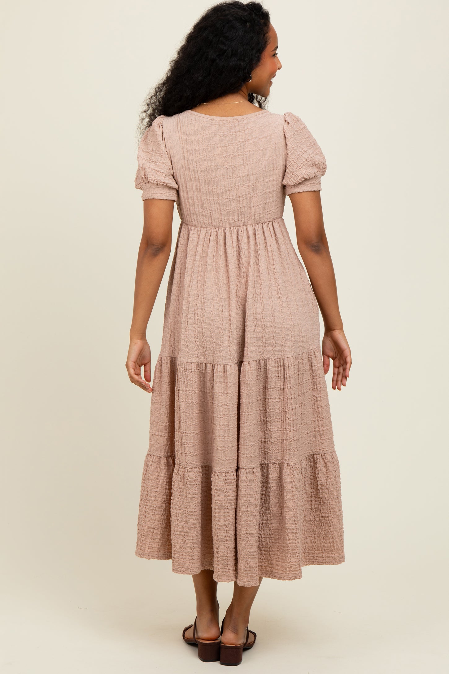 woman wearing a light beige tiered maxi dress with puff sleeves, shown from the back