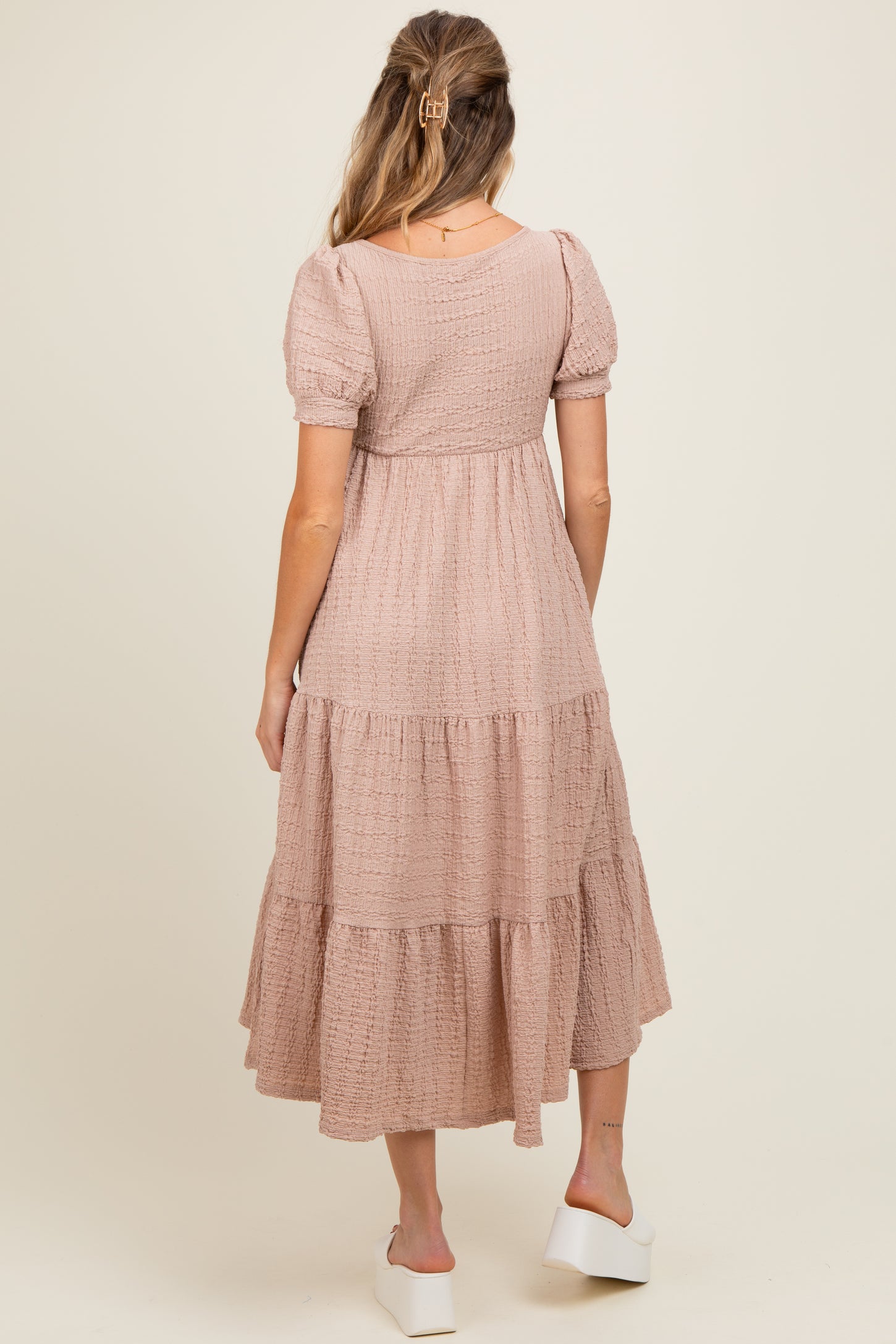 woman wearing a dusty pink maternity dress with puff sleeves and tiered skirt, showing the back view