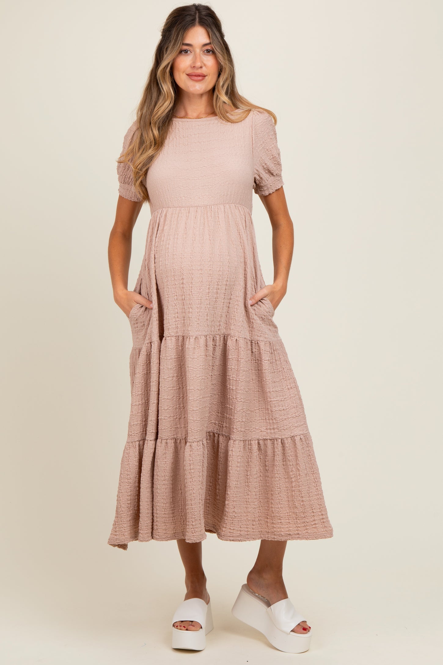 woman wearing a pink maternity dress with short puff sleeves and pockets, featuring a tiered skirt and visible baby bump