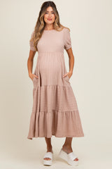 woman wearing a pink maternity dress with short puff sleeves and pockets, featuring a tiered skirt and visible baby bump