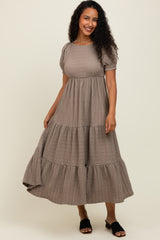 woman wearing a taupe tiered puff sleeve maxi dress with a textured fabric and black slide sandals