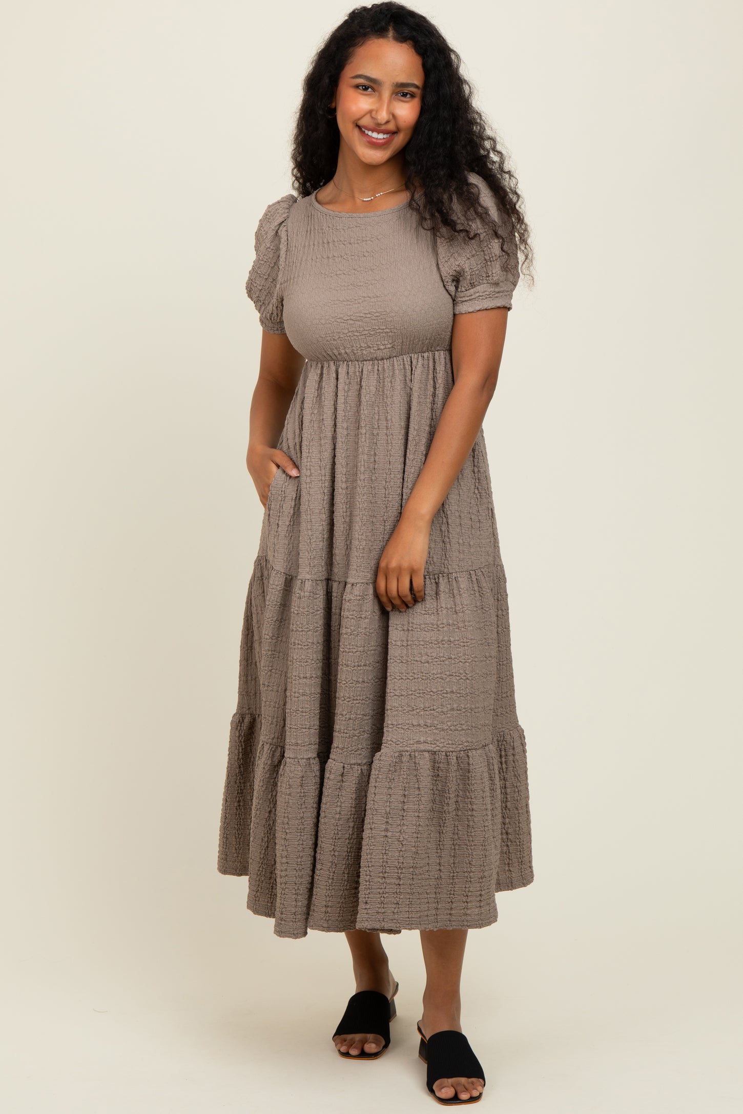 woman wearing a taupe puff sleeve tiered maxi dress with pockets and a textured finish