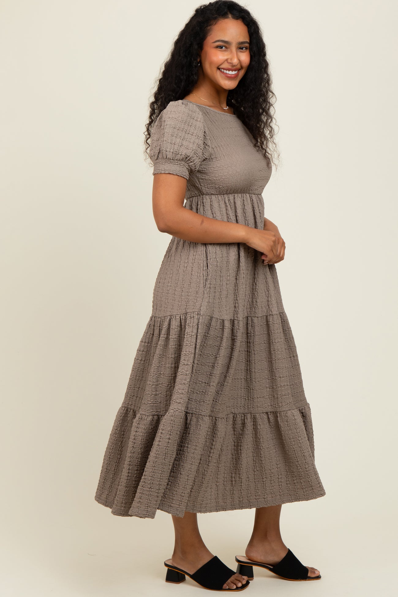 woman wearing a taupe tiered maxi dress with short puff sleeves and a fitted bodice