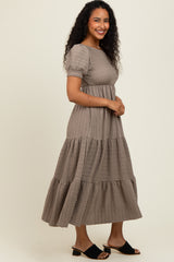 woman wearing a taupe tiered maxi dress with short puff sleeves and a fitted bodice