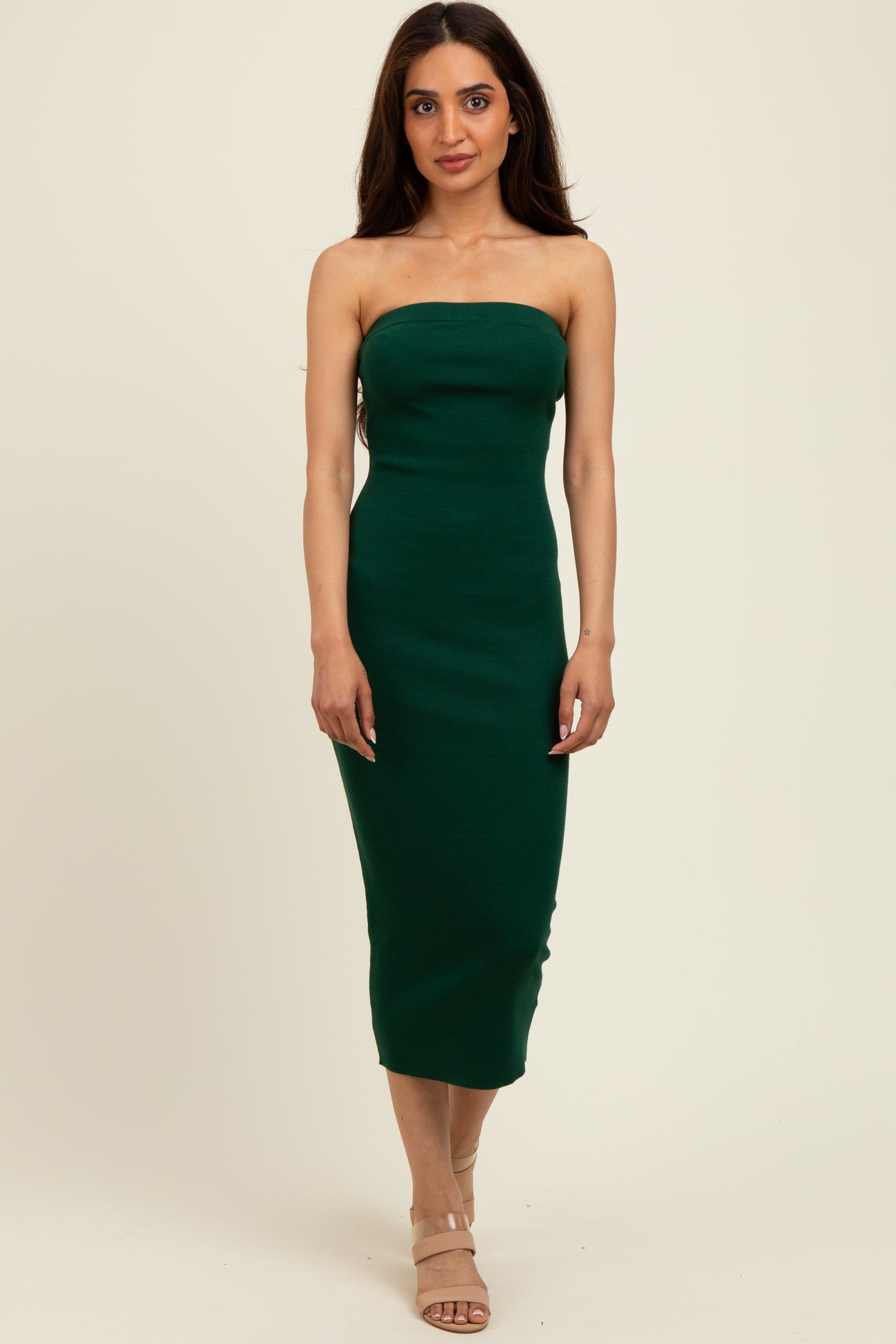 woman wearing a dark green strapless bodycon midi dress and beige heels