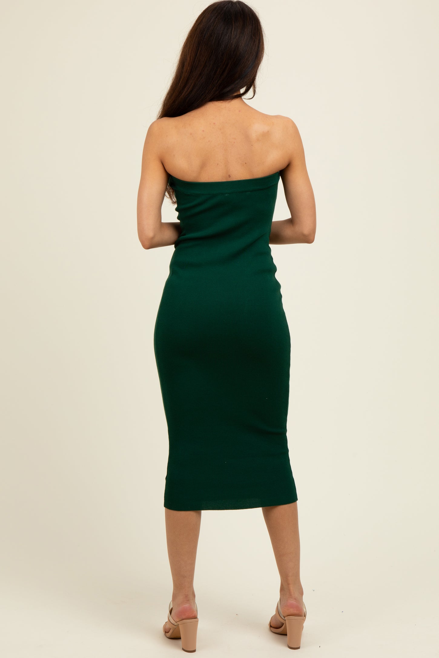 woman wearing a form-fitting dark green strapless midi dress standing with her back to the camera