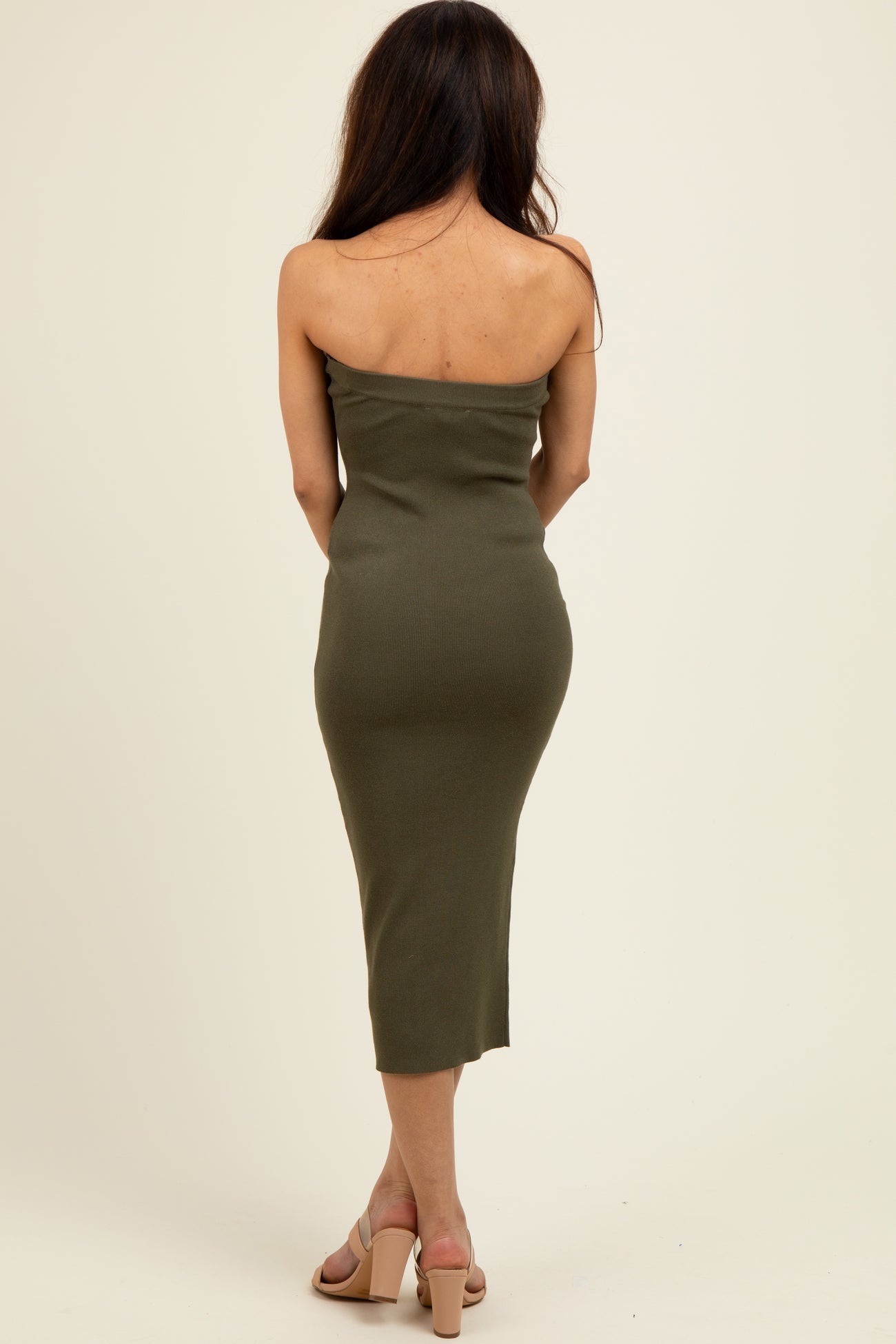 woman wearing an olive green strapless midi dress and beige heeled sandals, view from the back