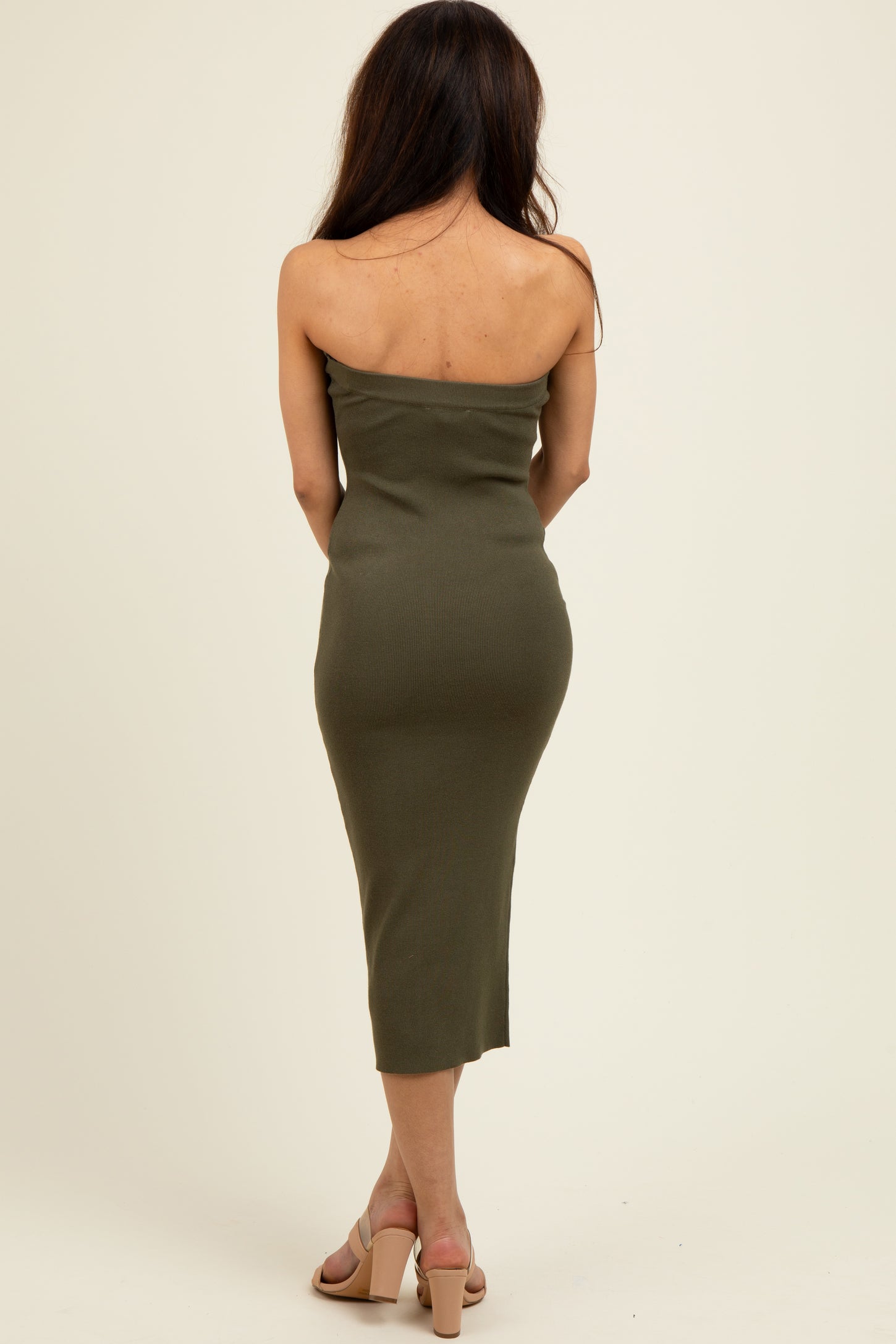 woman wearing an olive green strapless midi dress and beige heeled sandals, view from the back