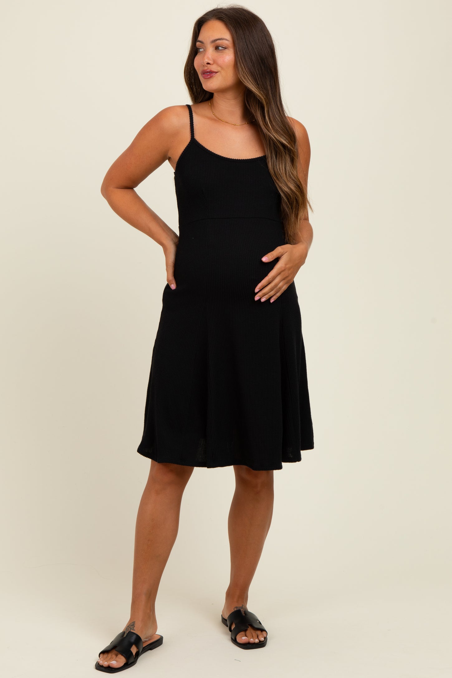 woman wearing a black maternity dress with adjustable straps and a flared skirt, holding her baby bump