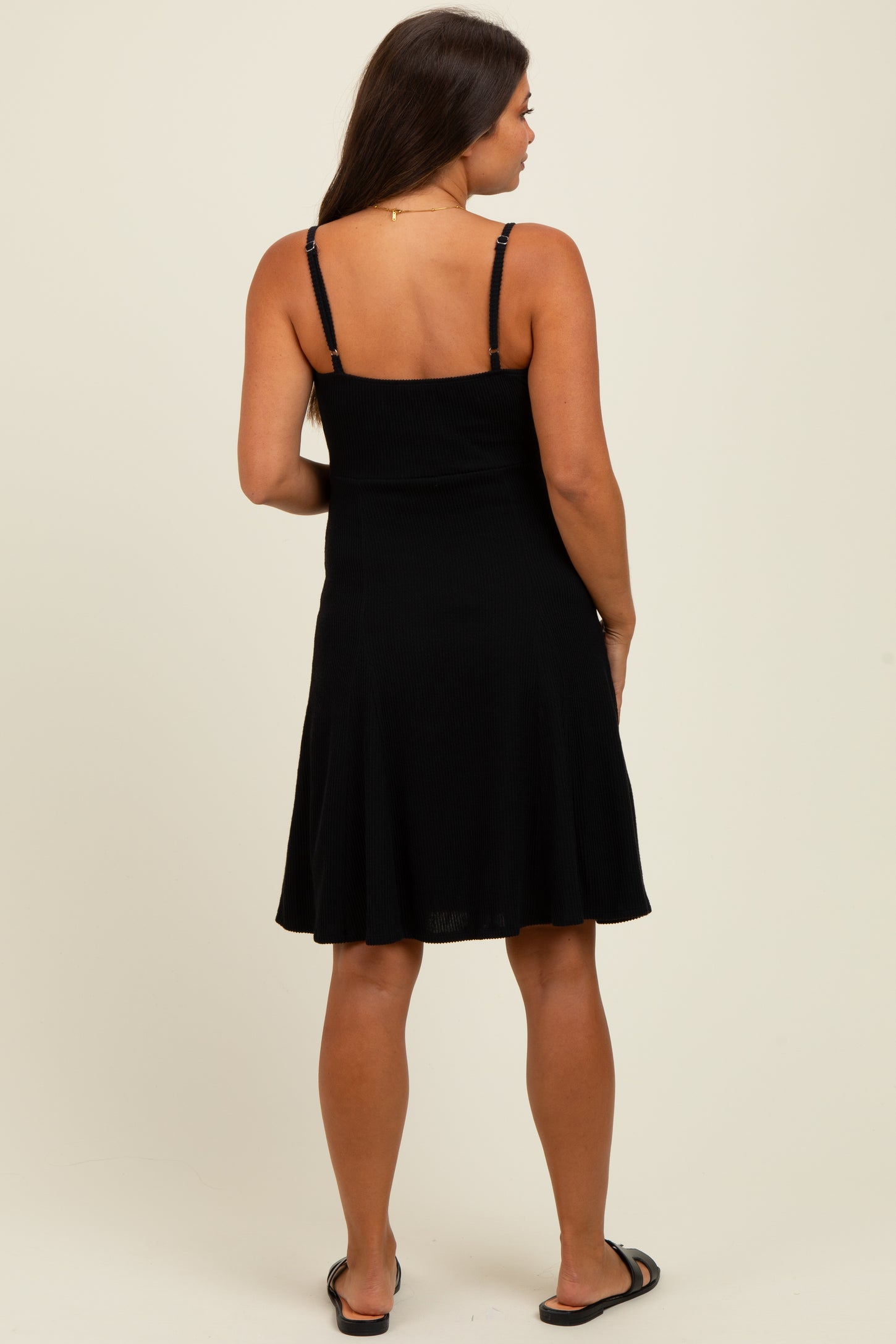 woman wearing a black spaghetti strap maternity dress, showing a flared skirt and styled for comfort during pregnancy