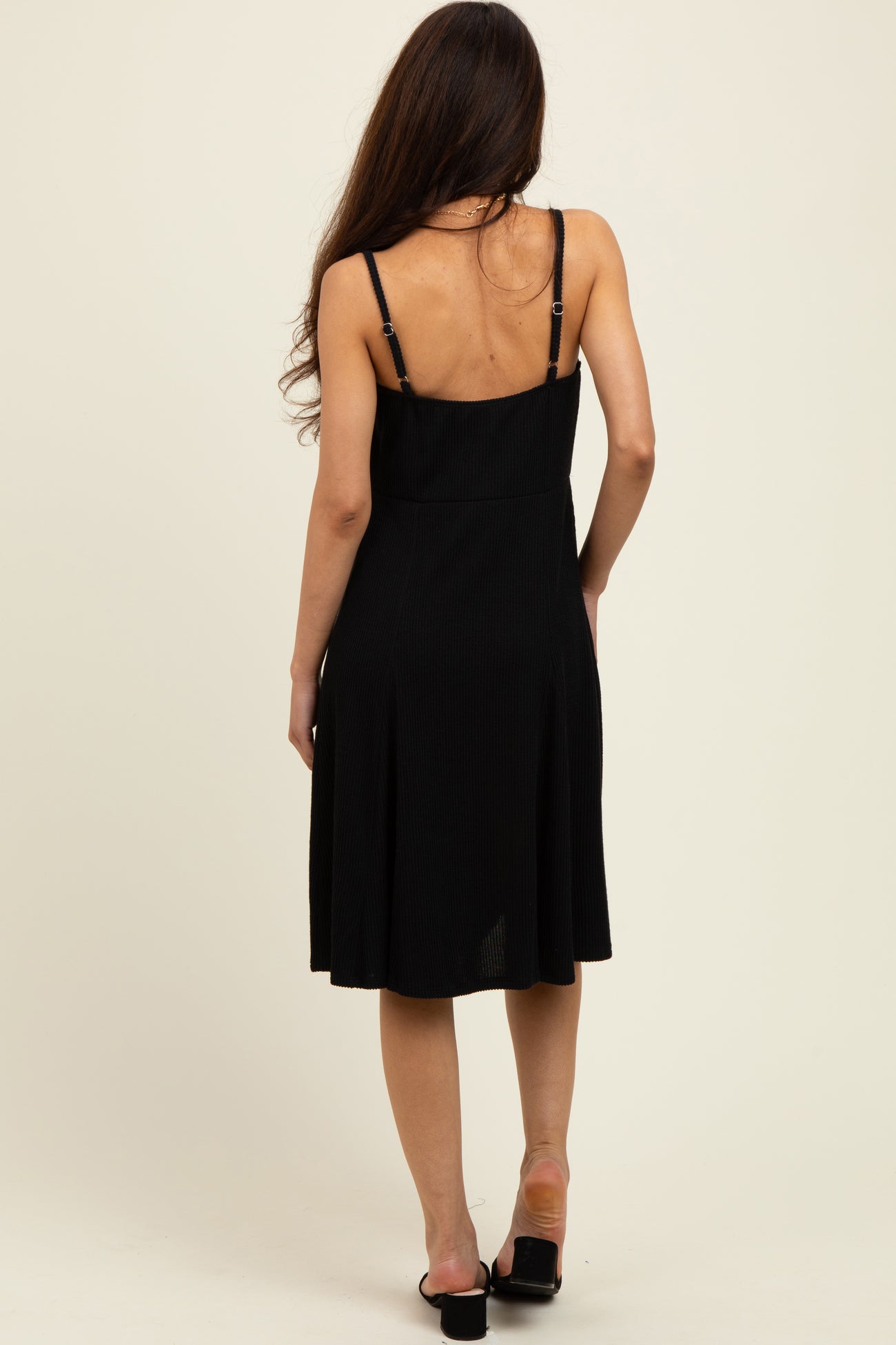 woman wearing a black ribbed sundress with adjustable straps, showing the back view and flowing skirt