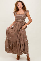 woman wearing a brown floral maxi dress with ruffle sleeves and a smocked bodice, standing against a neutral background