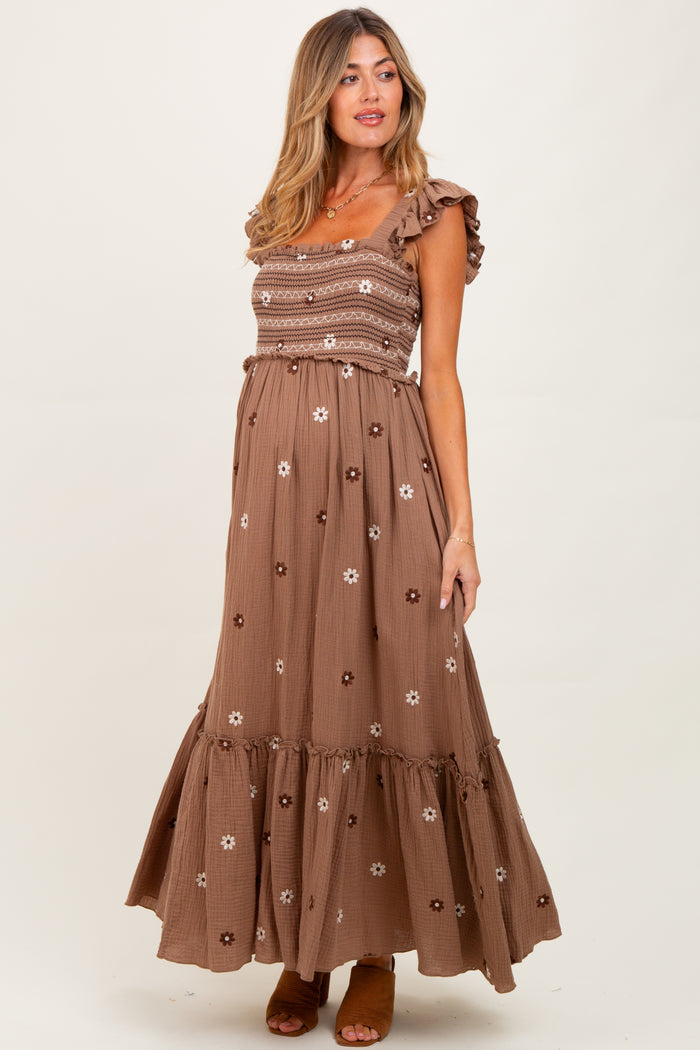 woman wearing a brown floral print maternity maxi dress with ruffled straps and a smocked bodice, showcasing her baby bump