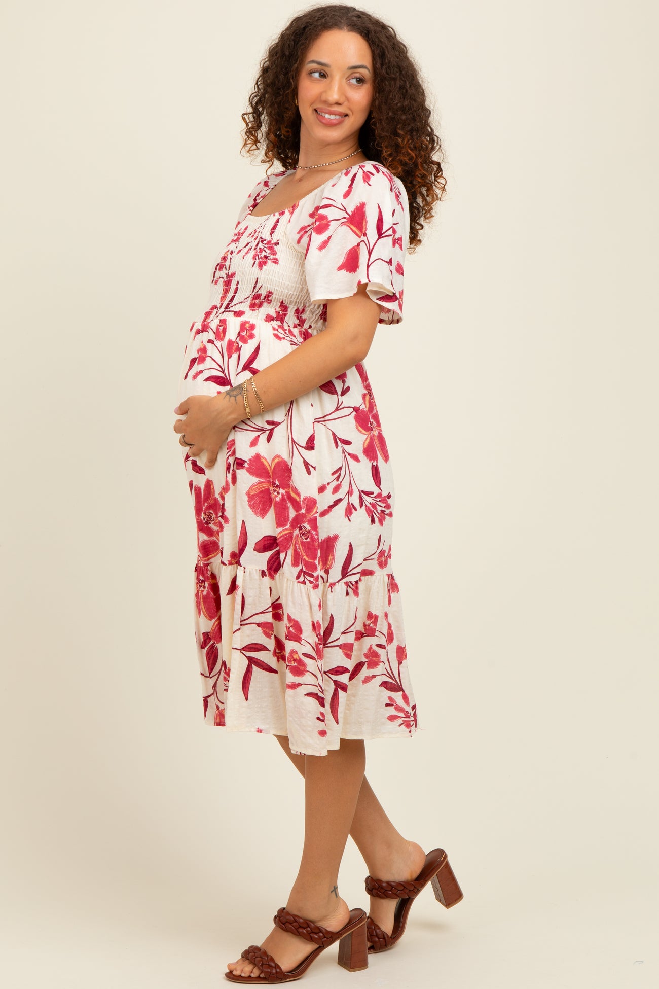 woman wearing a white maternity dress with red floral print and holding her baby bump