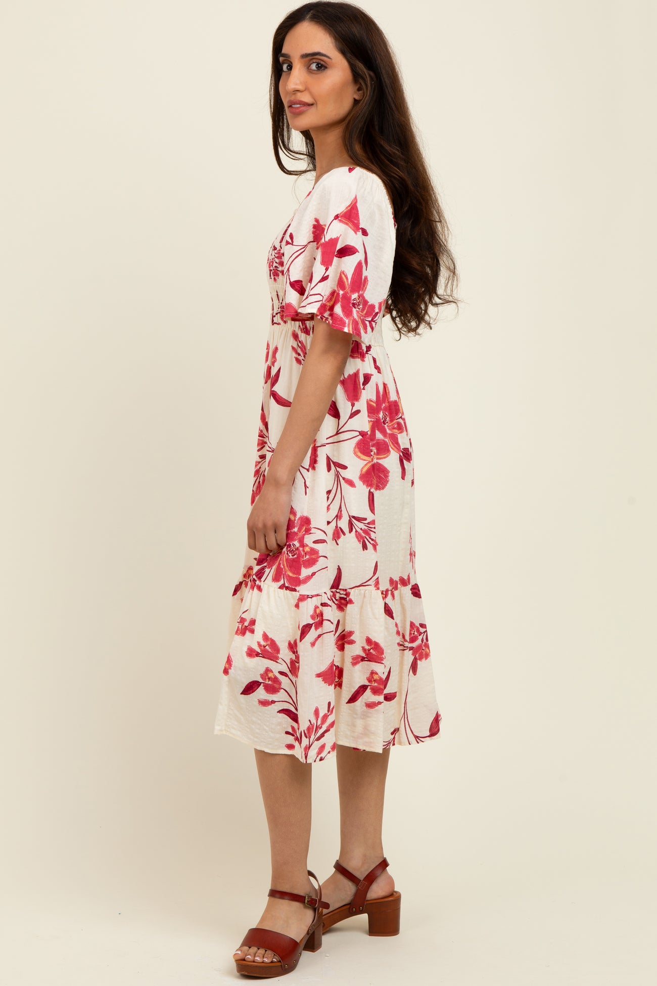 woman wearing a cream floral midi dress with pink flowers and short puff sleeves, standing sideways with a casual pose