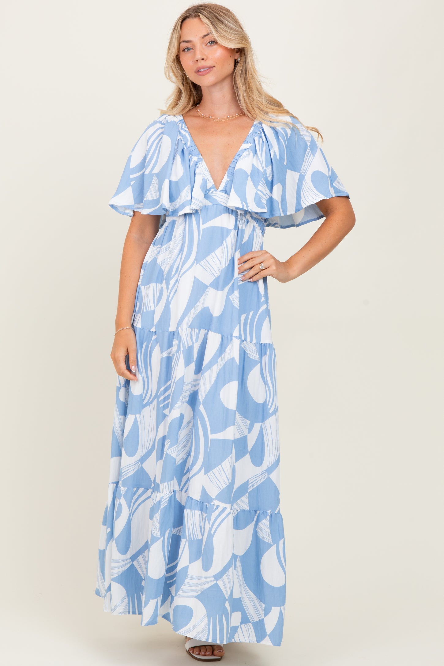 woman wearing a blue patterned maxi dress with flutter sleeves and a deep v-neckline