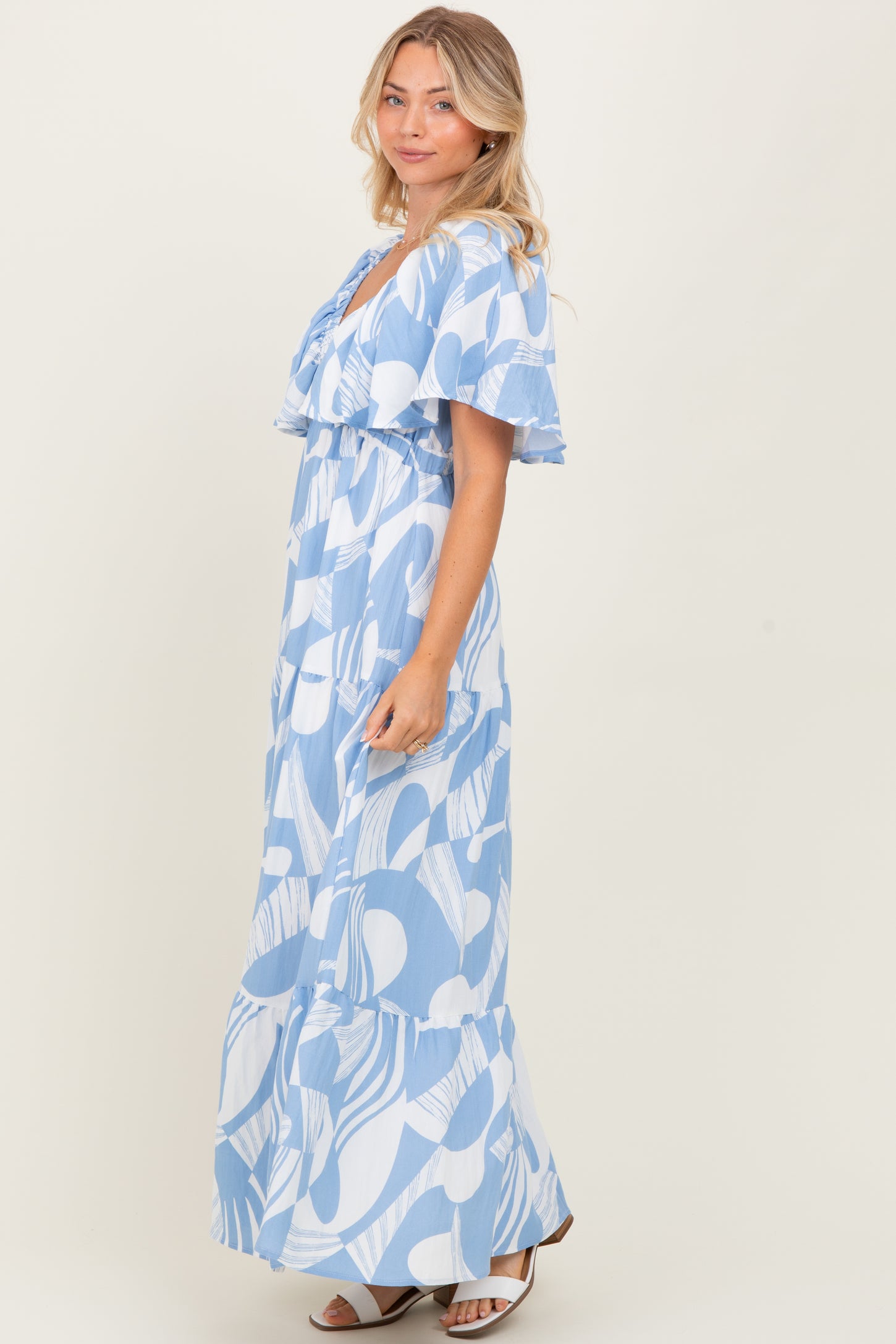 woman wearing a blue and white patterned maxi dress with flutter sleeves and a tiered skirt