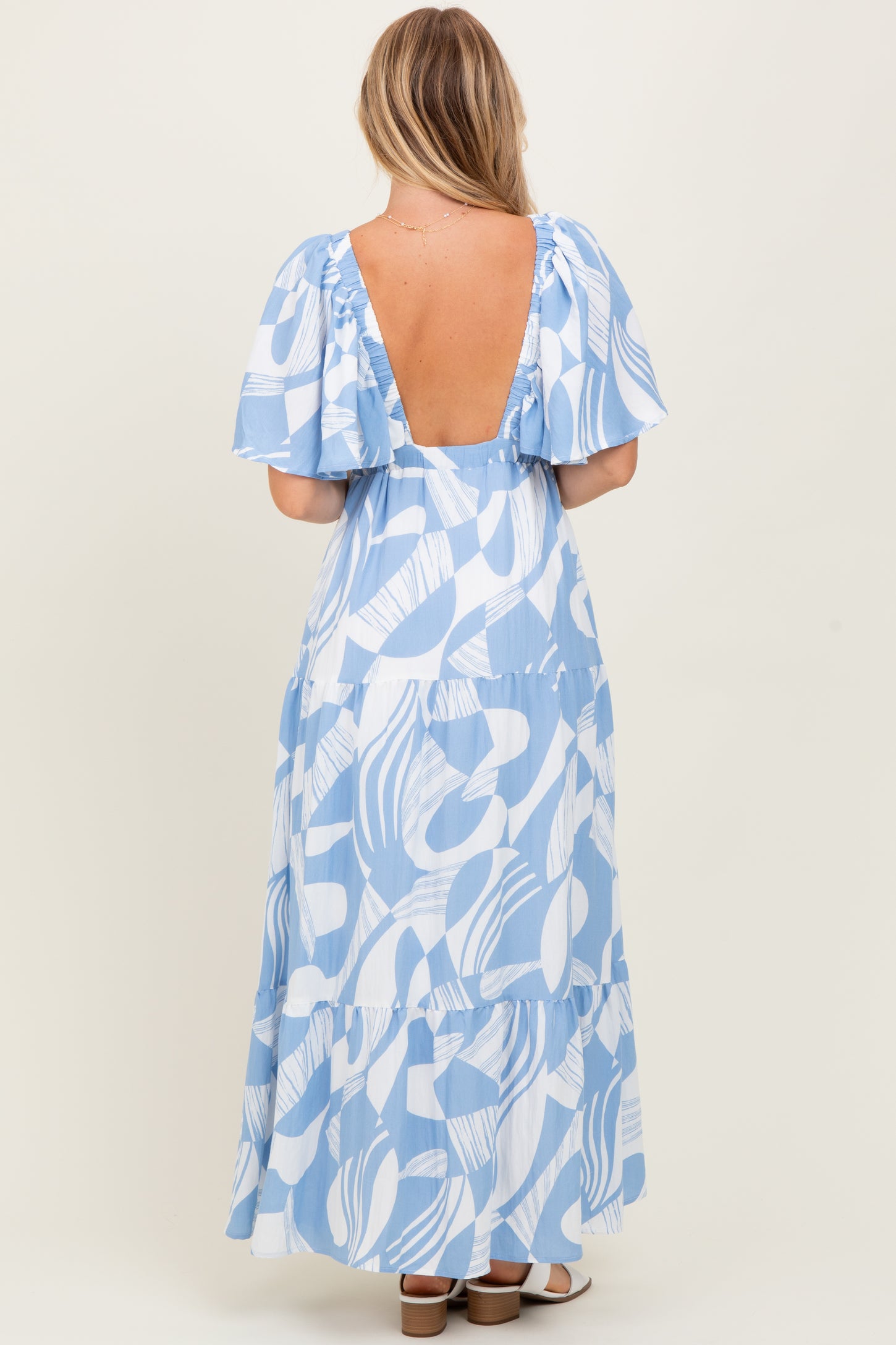 woman wearing a blue leaf print maxi dress with puff sleeves and a deep back neckline