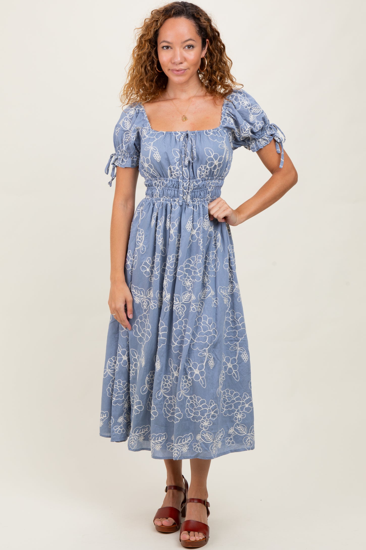 woman wearing a blue floral midi dress with puff sleeves and a cinched waist, standing against a neutral background