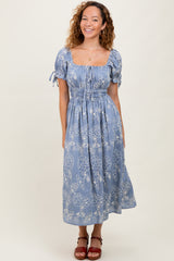 woman wearing a blue floral midi dress with puff sleeves and a cinched waist, smiling and standing against a neutral background
