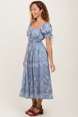 woman wearing a light blue midi dress with puff sleeves and floral embroidery, smiling while standing sideways