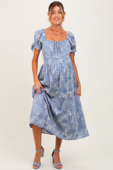 woman wearing a blue floral maternity dress with puff sleeves and a baby bump visible.