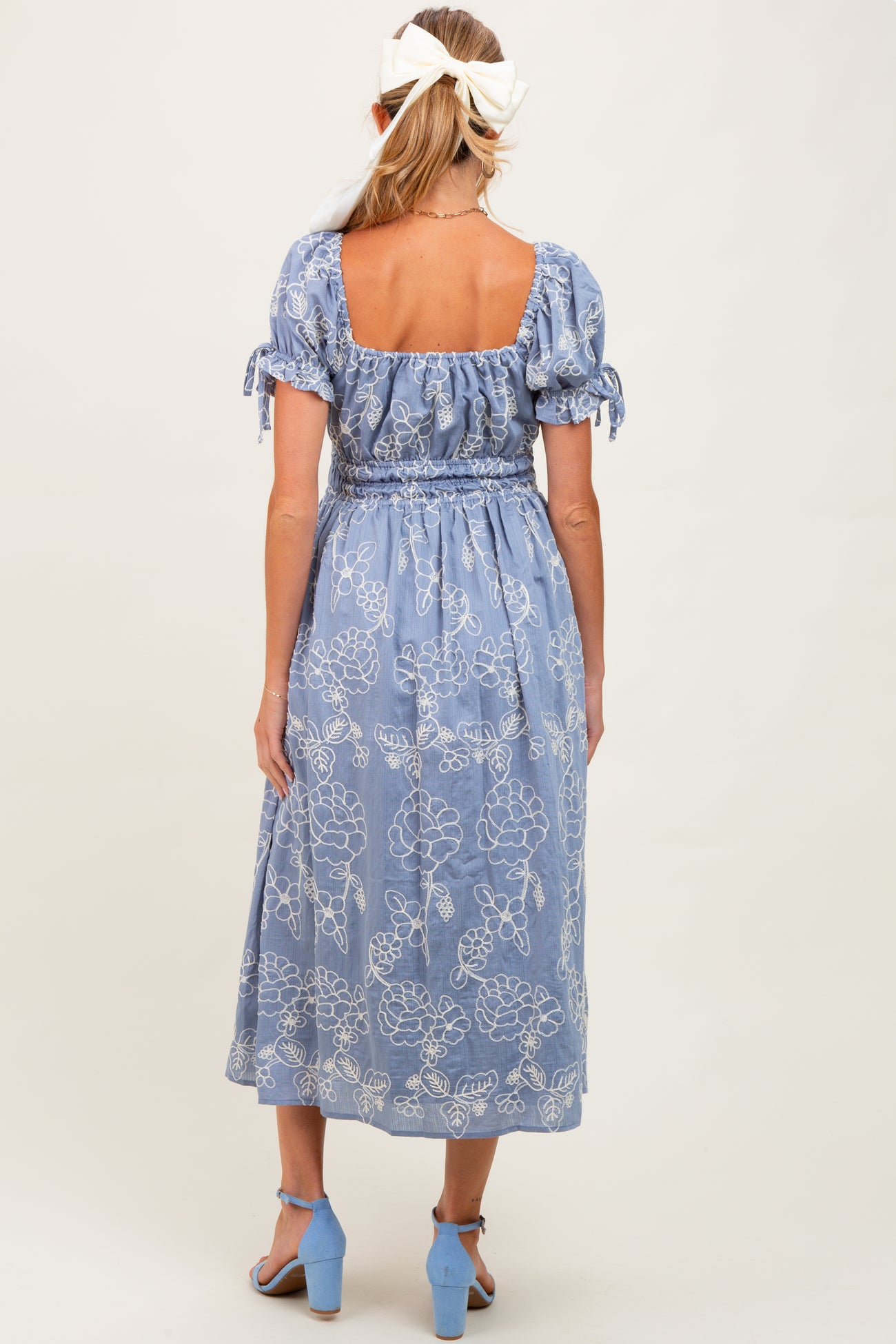 woman wearing a light blue maternity maxi dress with floral patterns and short puff sleeves, showing a baby bump