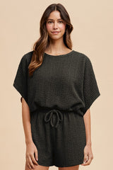 woman wearing a dark green short sleeve knit romper with a drawstring waist
