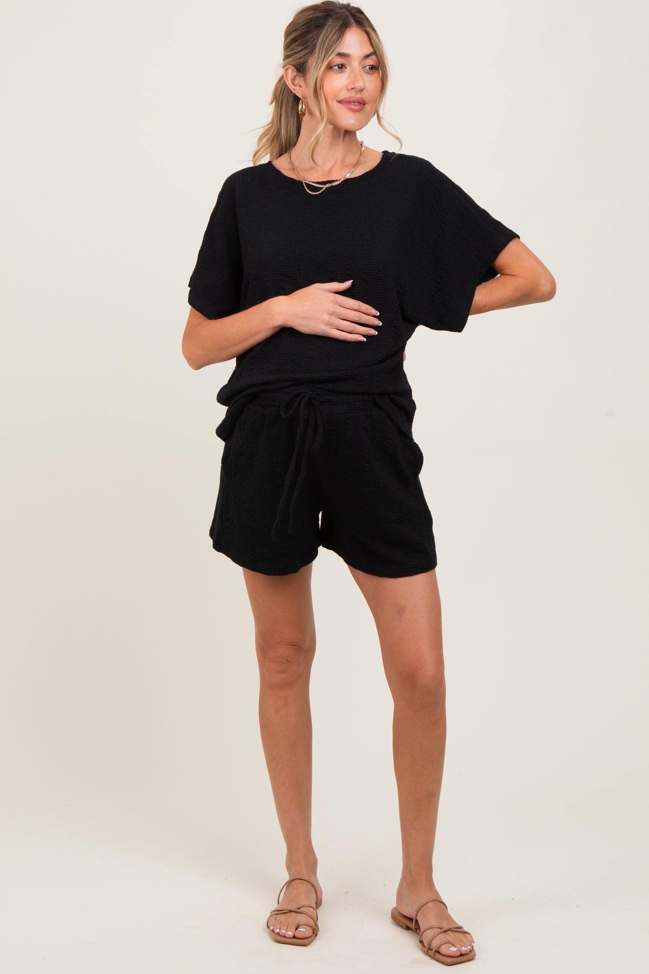 woman wearing a black maternity top and matching shorts, hands on her baby bump