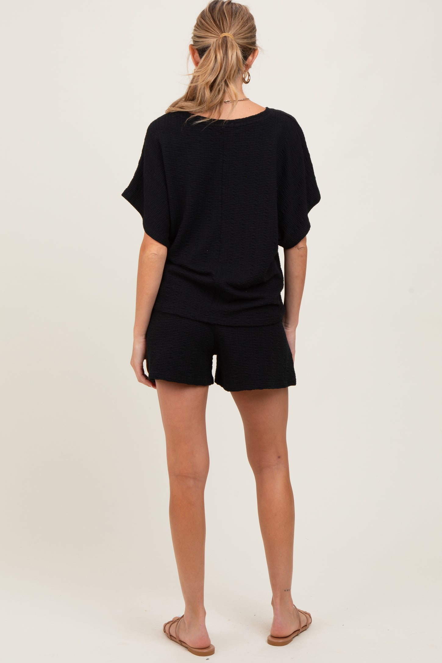 woman wearing a black maternity short set, with a loose top and shorts, viewed from the back