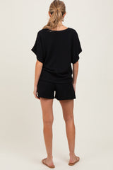 woman wearing a black maternity short set, with a loose top and shorts, viewed from the back