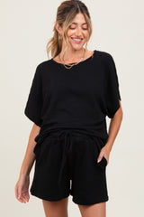 woman wearing a black short sleeve maternity top and matching shorts with a waist tie detail, smiling