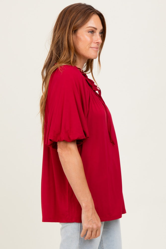 woman wearing a red short sleeve top with a lace-up neckline and relaxed fit, standing sideways against a neutral background