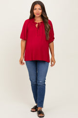 woman wearing a burgundy maternity top with a tie neckline and puff sleeves, paired with blue jeans and black sandals, showing a baby bump