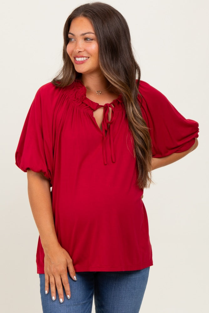 woman wearing a red maternity top with a tie neck and puff sleeves, showcasing her baby bump