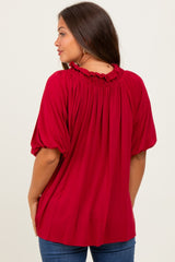 woman wearing a burgundy maternity top with a ruffled neckline and puff sleeves, styled with jeans